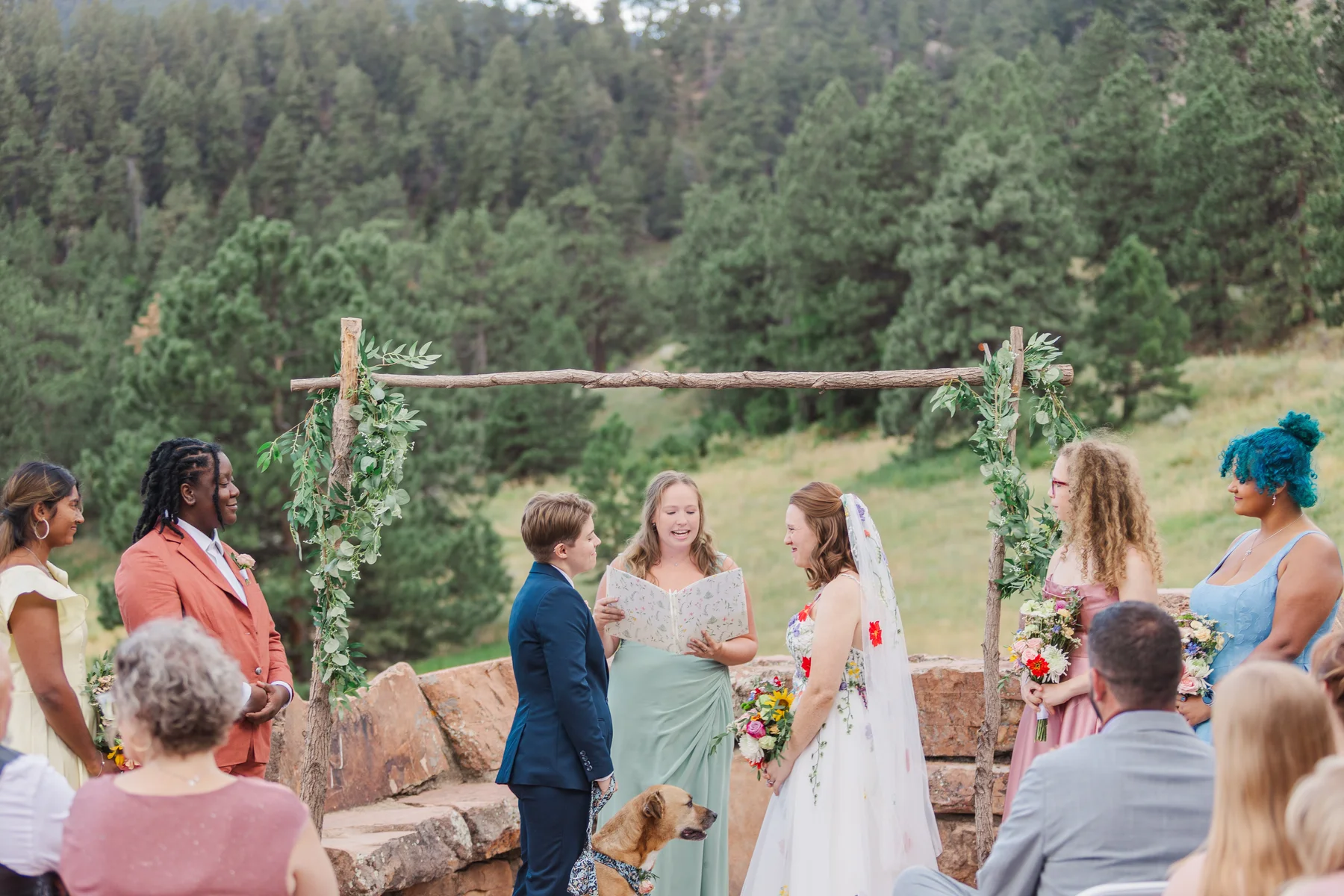 Sydney and Hannah Rusow exchange vows under a rustic wood arch at Halfway House in Boulder, CO.