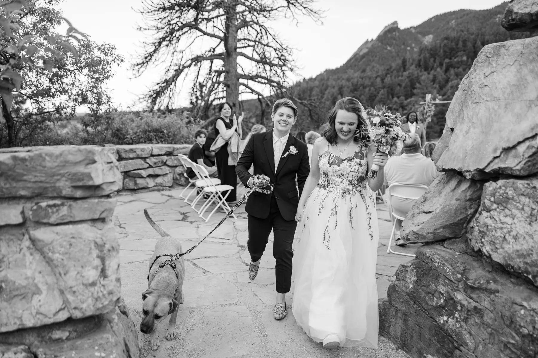 Sydney and Hannah Rusow walk hand-in-hand with their dog after their ceremony at Halfway House in Boulder, CO.