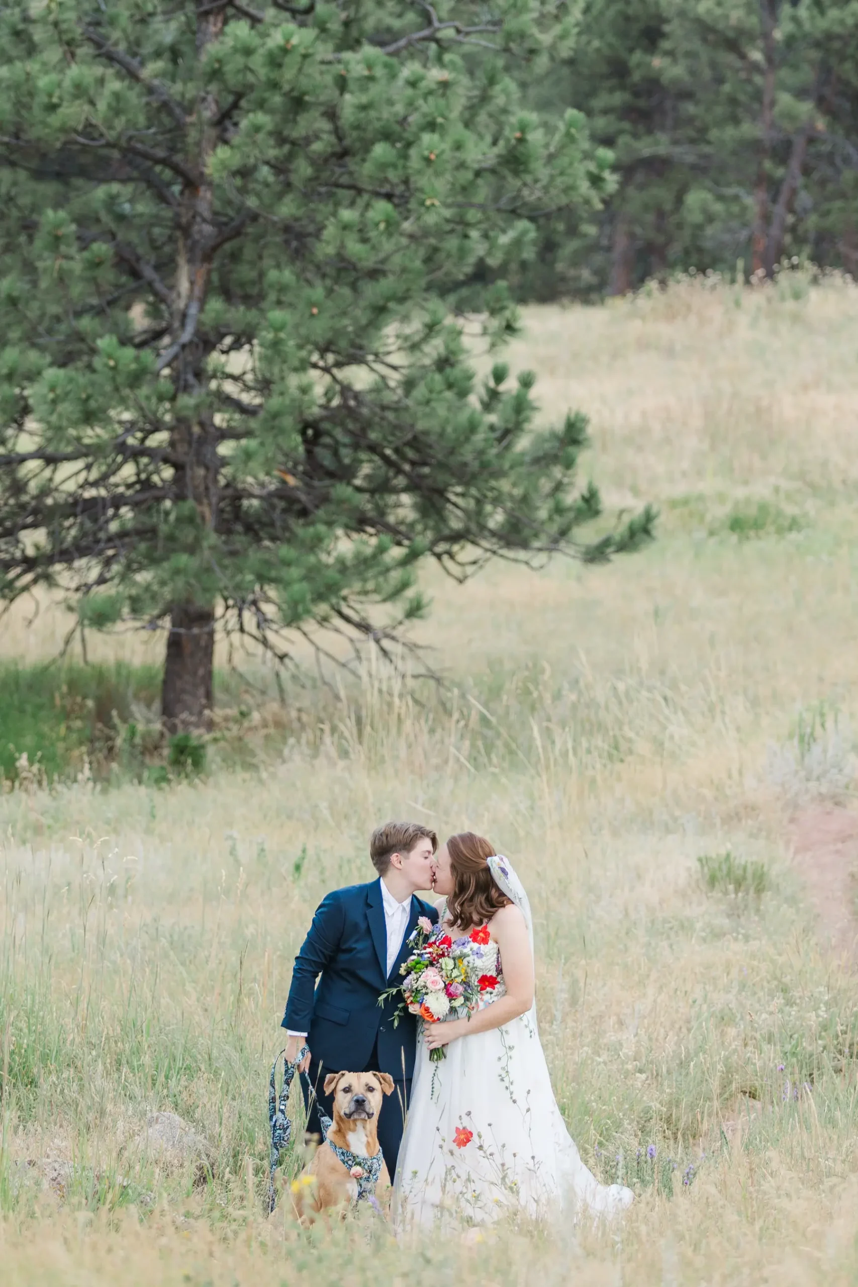 Sydney and Hannah Rusow share a first kiss in a golden meadow with their dog at Halfway House in Boulder, CO.