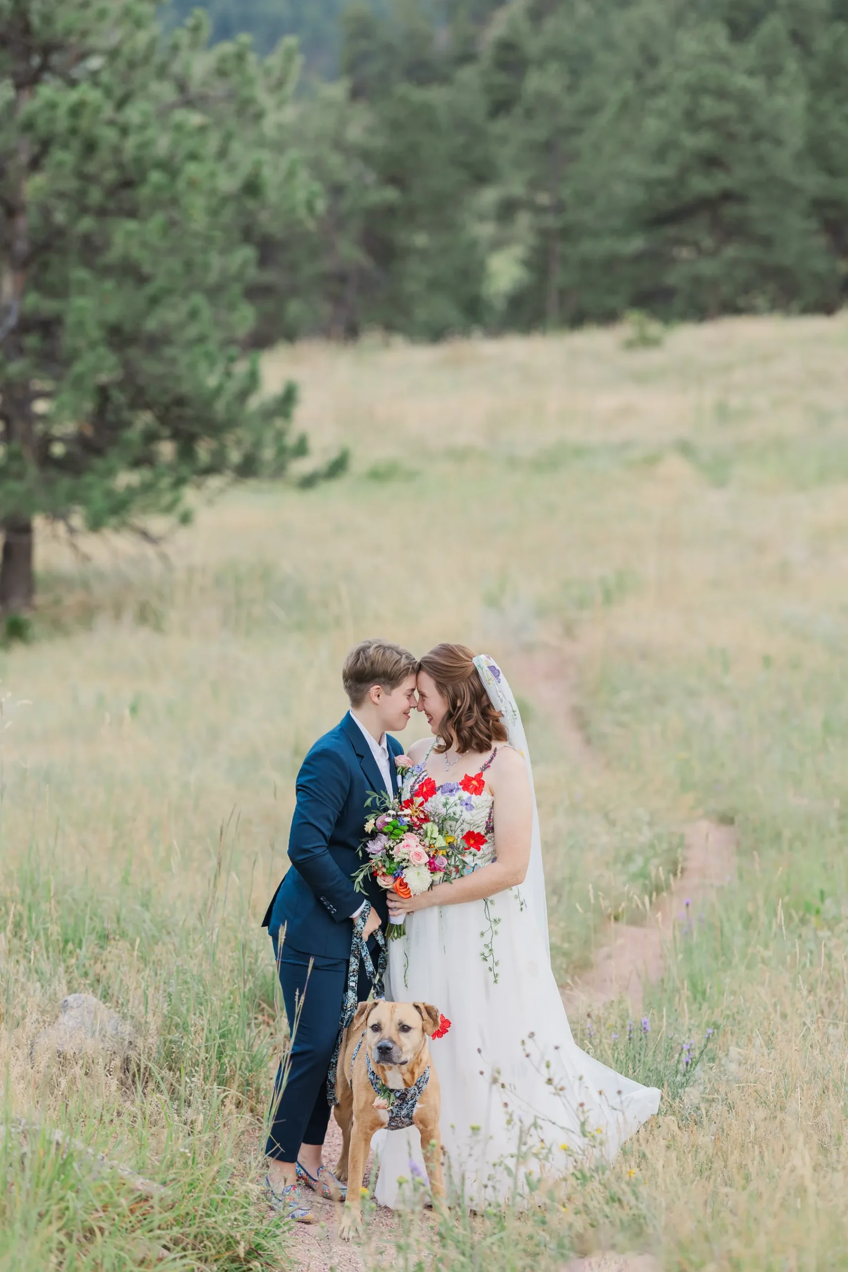 Sydney and Hannah Rusow touch foreheads in a sunny meadow with their dog at Halfway House in Boulder, CO.