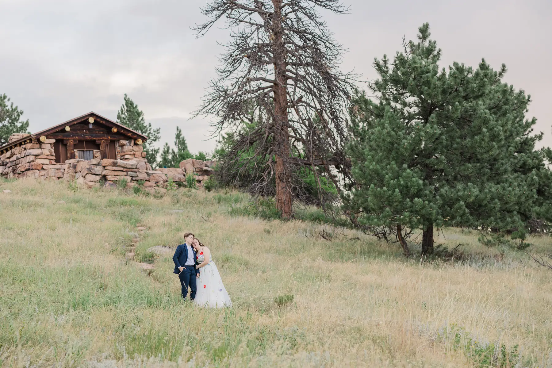 Sydney and Hannah Rusow walk through a grassy hillside meadow near a stone lodge at Halfway House in Boulder, CO.