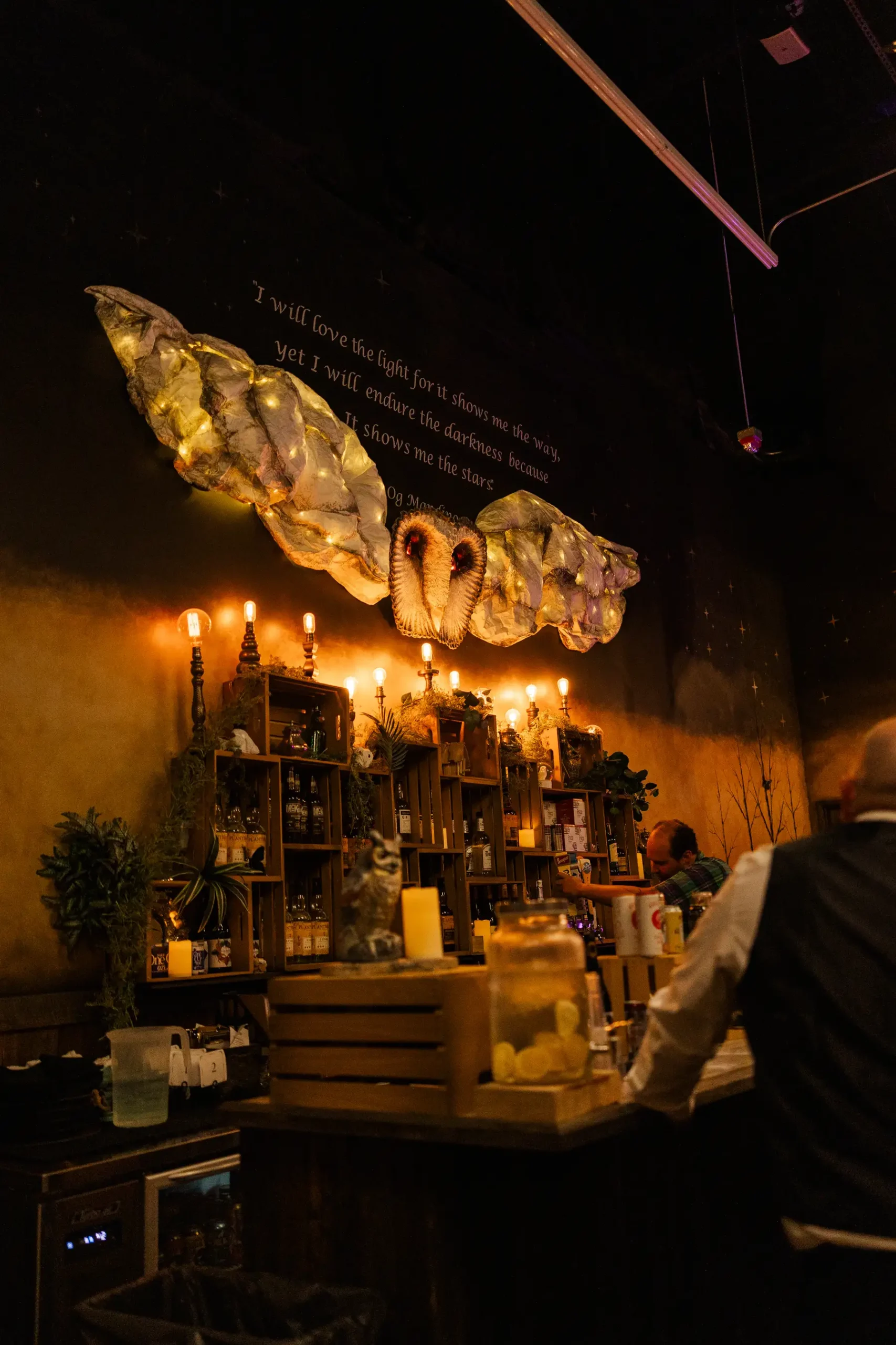 Dimly lit bar at Halfway House in Boulder, CO, decorated with fairy-lit wings and candles for Sydney and Hannah Rusow's wedding reception.