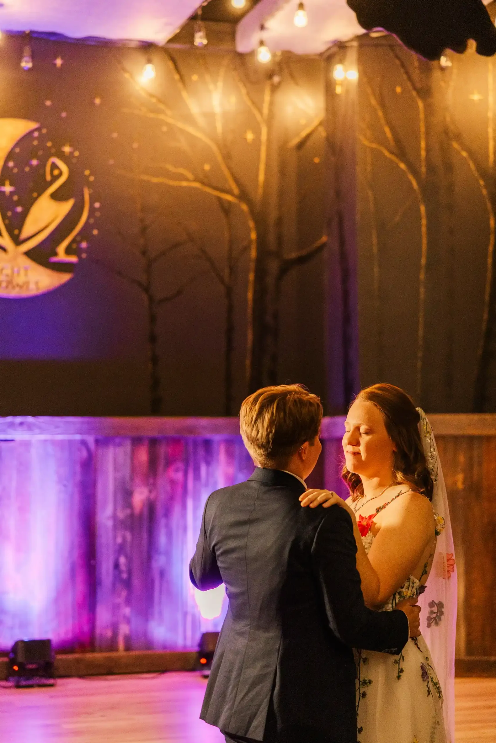 Sydney and Hannah Rusow share their first dance at Halfway House in Boulder, CO, surrounded by warm string lights.