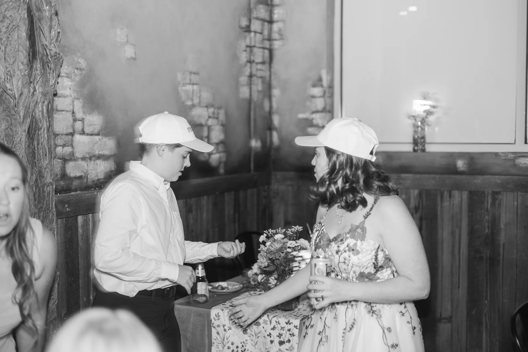 Guests in matching white baseball caps chat and laugh during Sydney and Hannah Rusow's reception at Halfway House in Boulder, CO.