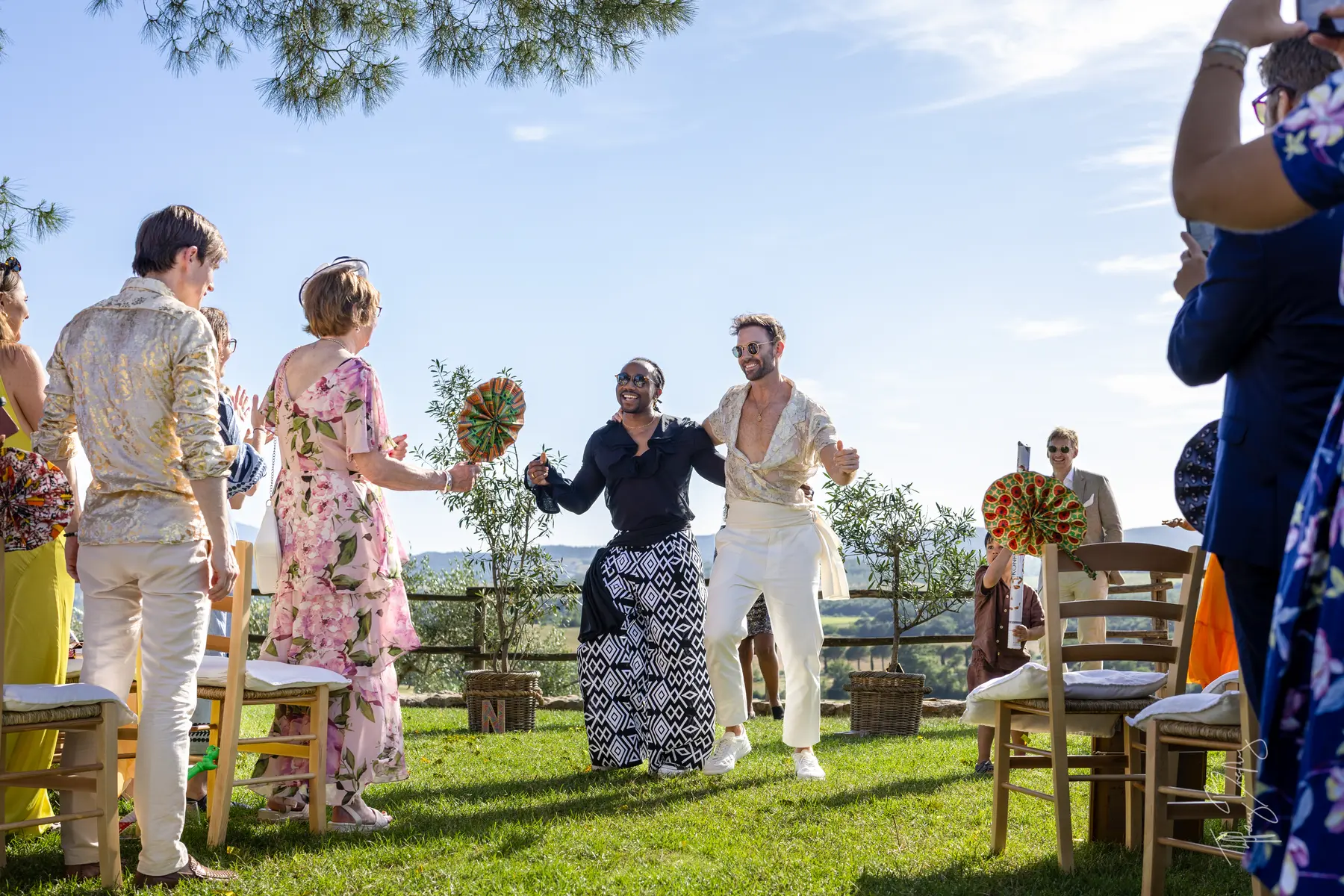 Two grooms dance joyfully down the aisle with guests at Conti di San Bonifacio Wine Resort in Tuscany, Italy.