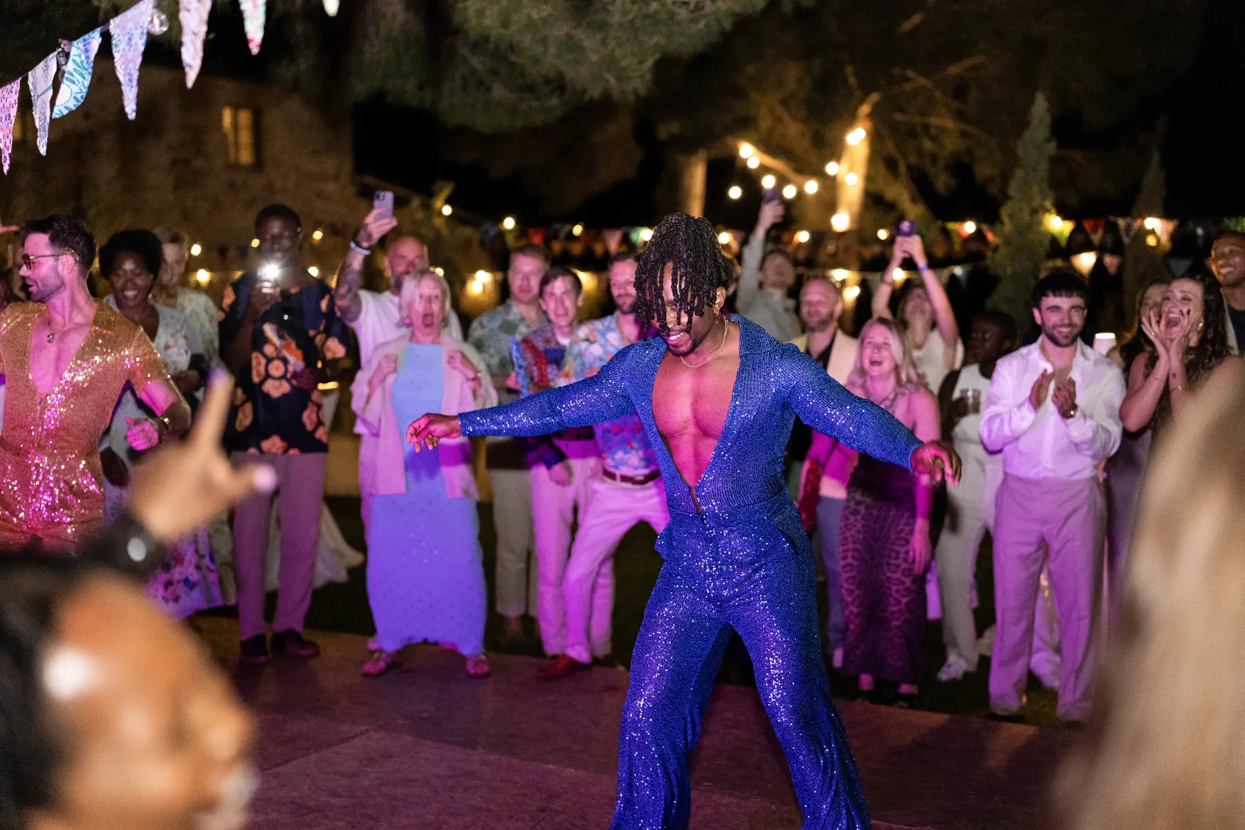 A performer in a sequined blue jumpsuit dances at an outdoor reception at Conti di San Bonifacio in Tuscany as guests cheer.