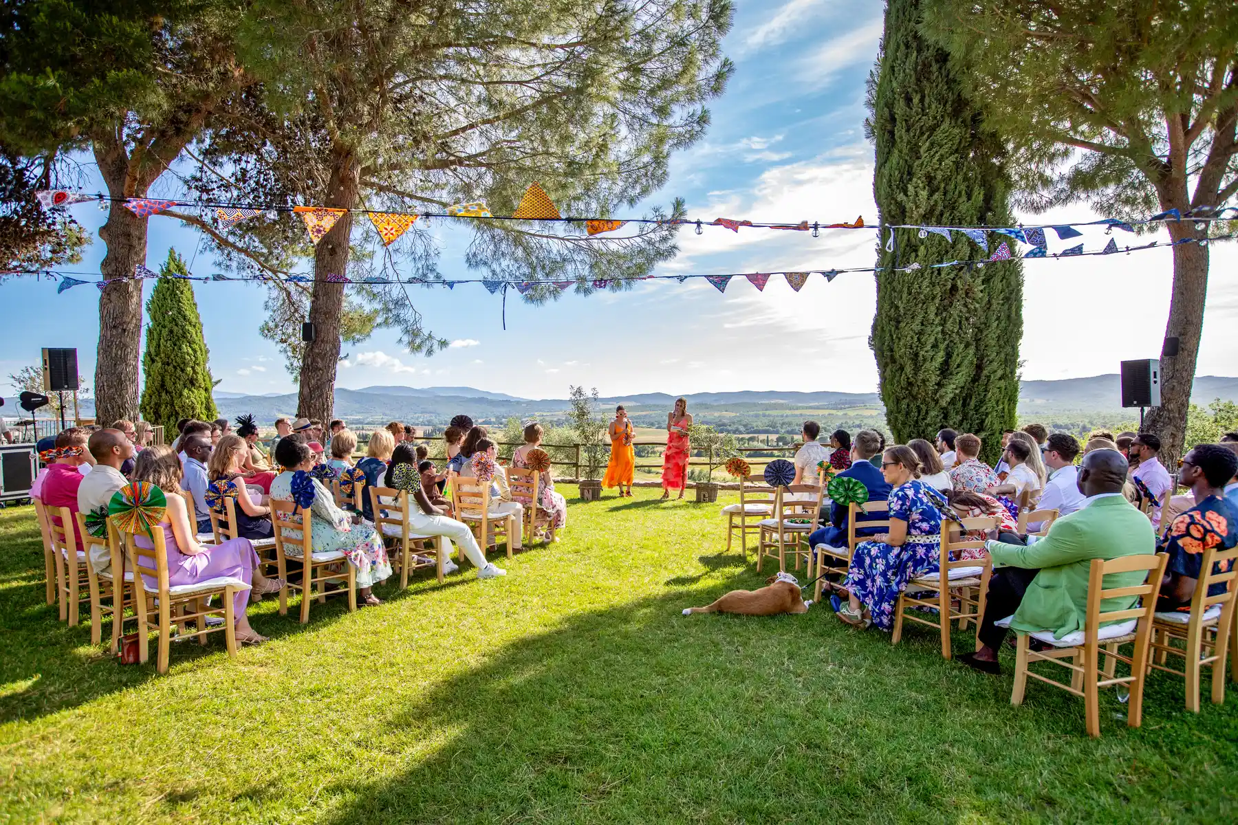 Guests seated on a sunny lawn watch two speakers during an outdoor ceremony at Conti di San Bonifacio in Tuscany.