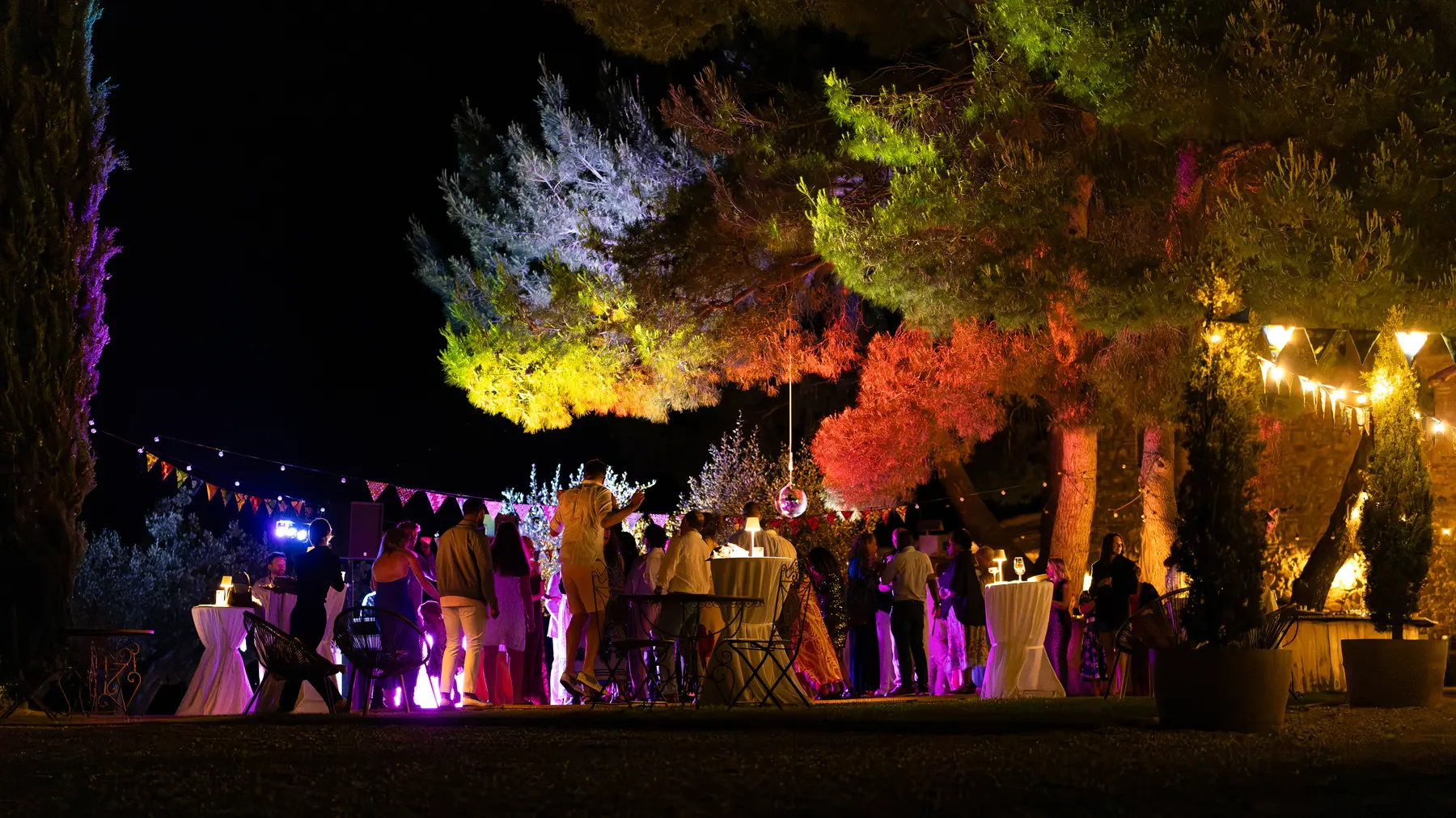 Guests mingle under colorful illuminated pine trees at an outdoor evening reception at Conti di San Bonifacio in Tuscany.