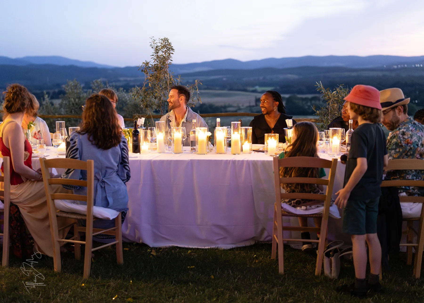 Guests and a groom share candlelit dinner at an outdoor round table at Conti di San Bonifacio Wine Resort in Tuscany.