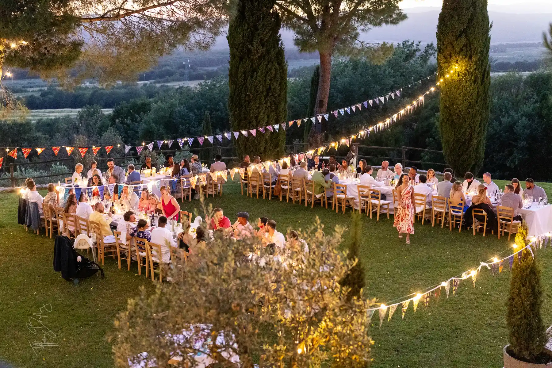 Wedding guests dine outdoors at dusk at Conti di San Bonifacio Wine Resort in Tuscany under string lights and colorful bunting.