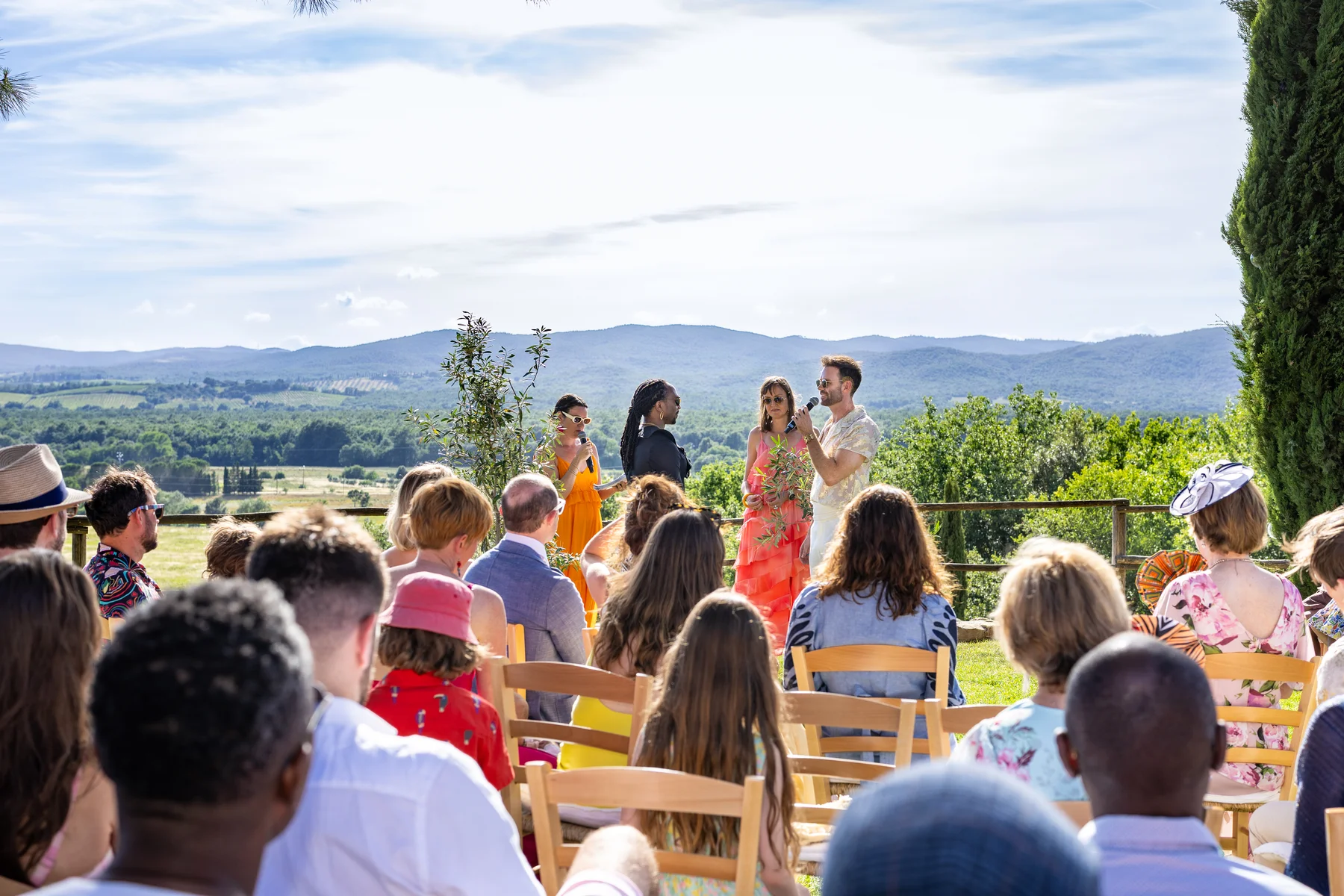 Two grooms exchange vows outdoors at Conti di San Bonifacio Wine Resort in Tuscany as guests look on beneath a sunny sky.