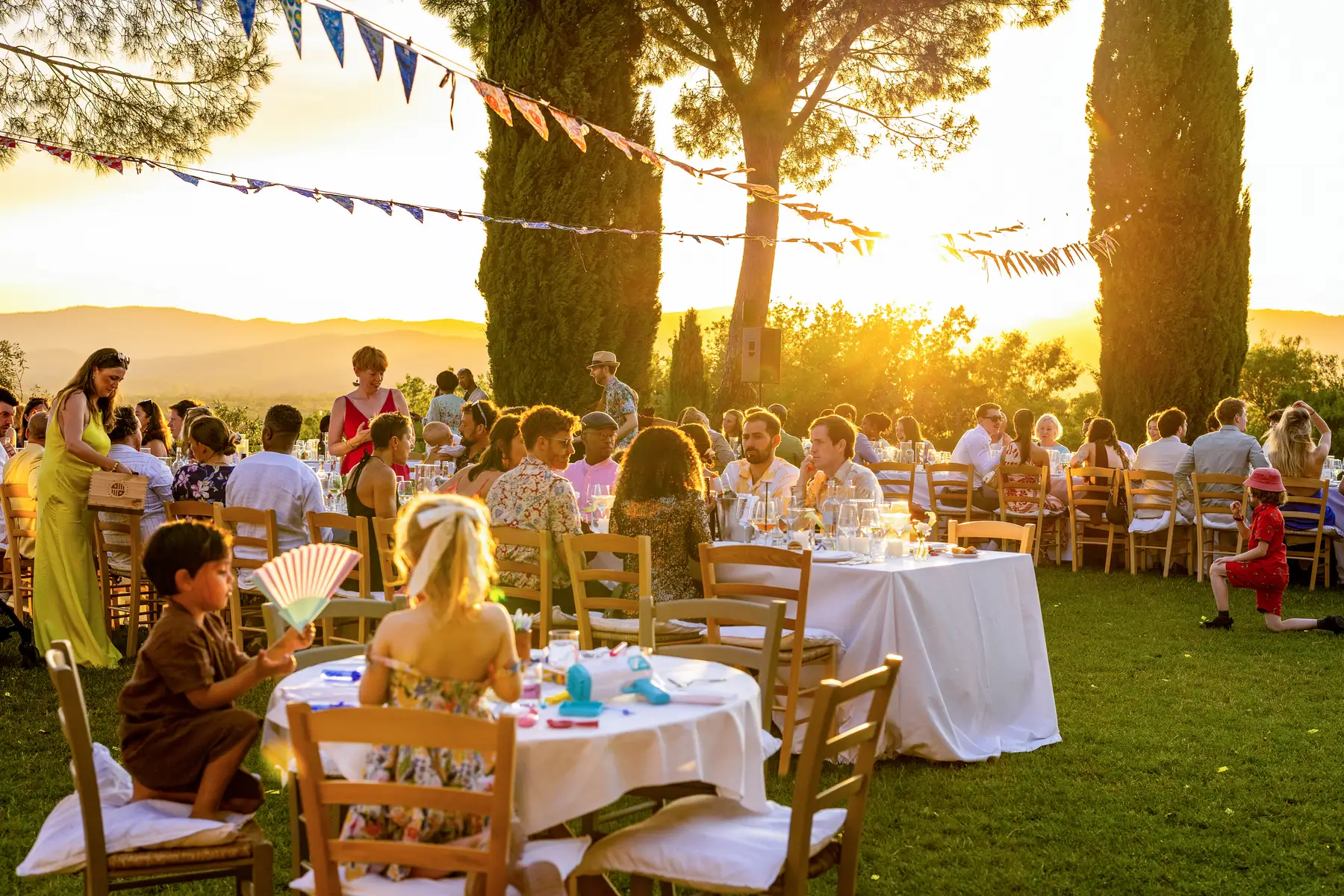 Wedding guests dine at white-clothed tables on the lawn at Conti di San Bonifacio Wine Resort in Tuscany at golden hour.