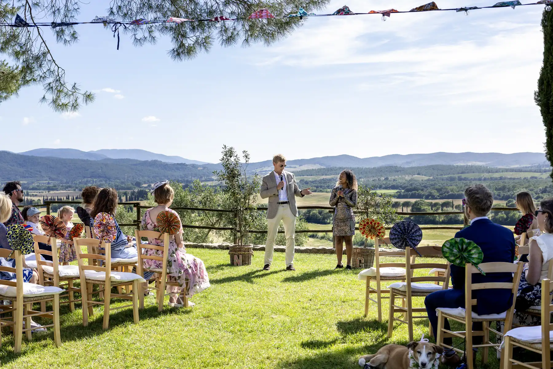Two grooms stand before seated guests during an outdoor ceremony at Conti di San Bonifacio Wine Resort in Tuscany.