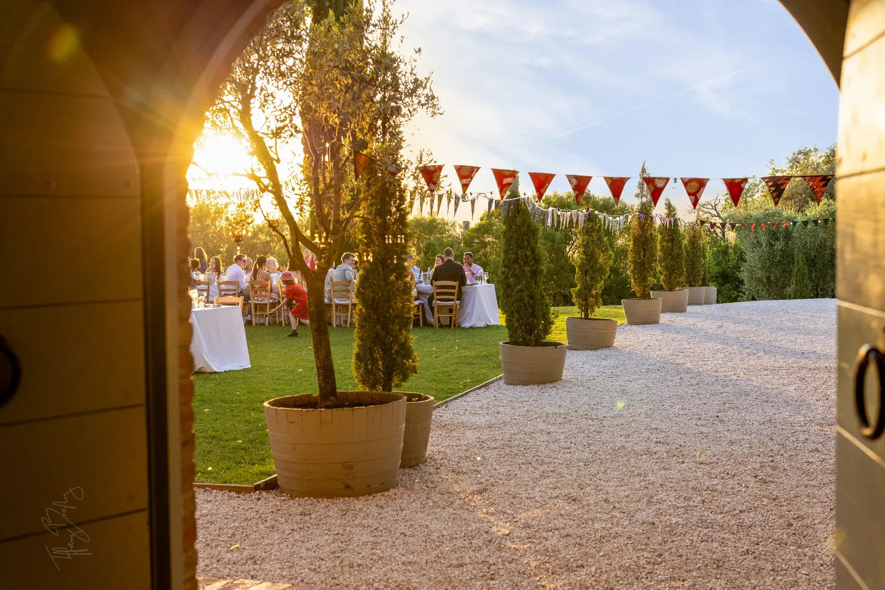 Guests dine al fresco at golden hour at Conti di San Bonifacio Wine Resort in Tuscany, with potted cypress trees and red bunting.
