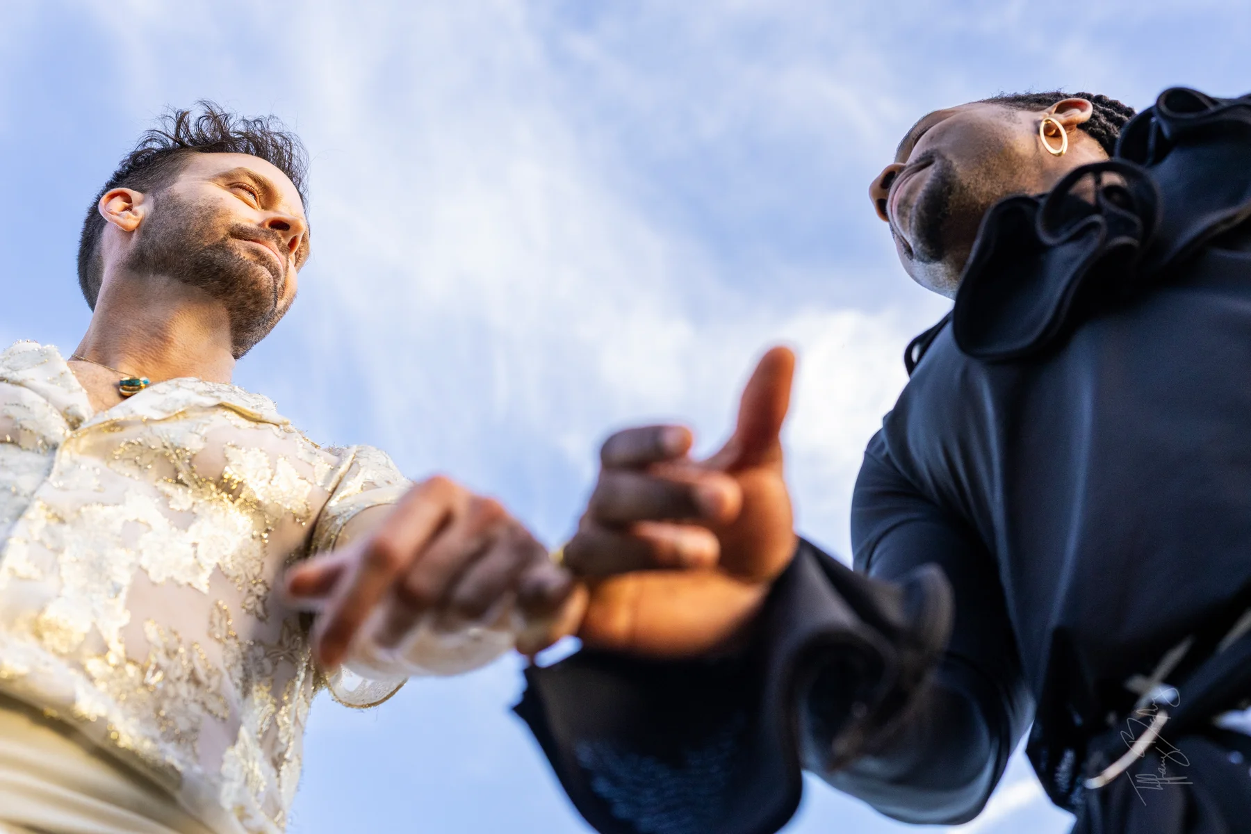 Low-angle view of two grooms holding hands beneath a blue sky at Conti di San Bonifacio Wine Resort in Tuscany.