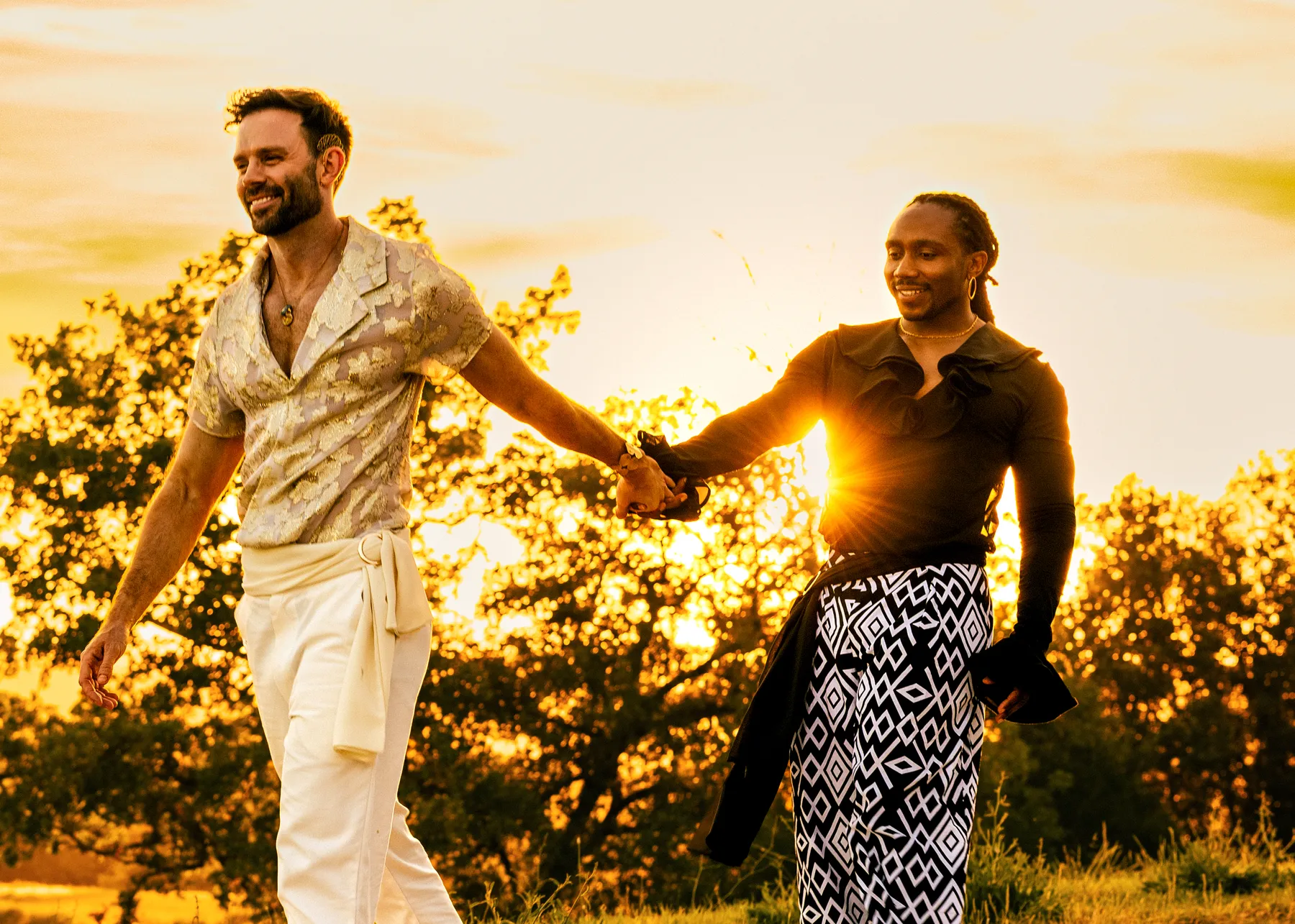 Two grooms hold hands and walk through golden sunset at Conti di San Bonifacio Wine Resort in Tuscany, Italy.