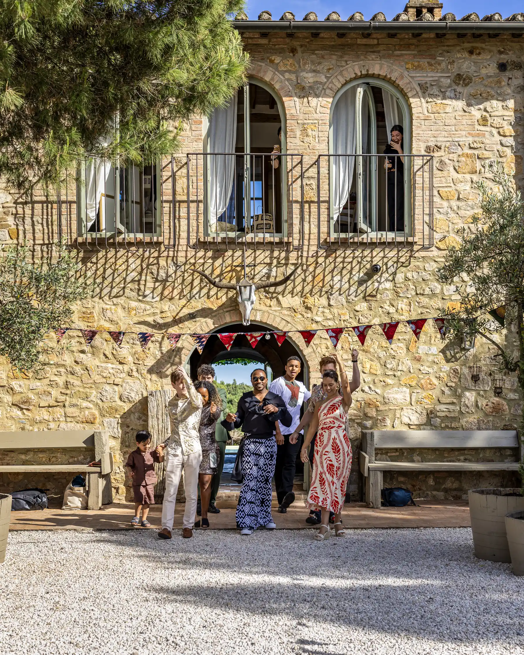 A joyful group dances through an arched stone gateway at Conti di San Bonifacio Wine Resort in Tuscany, Italy.