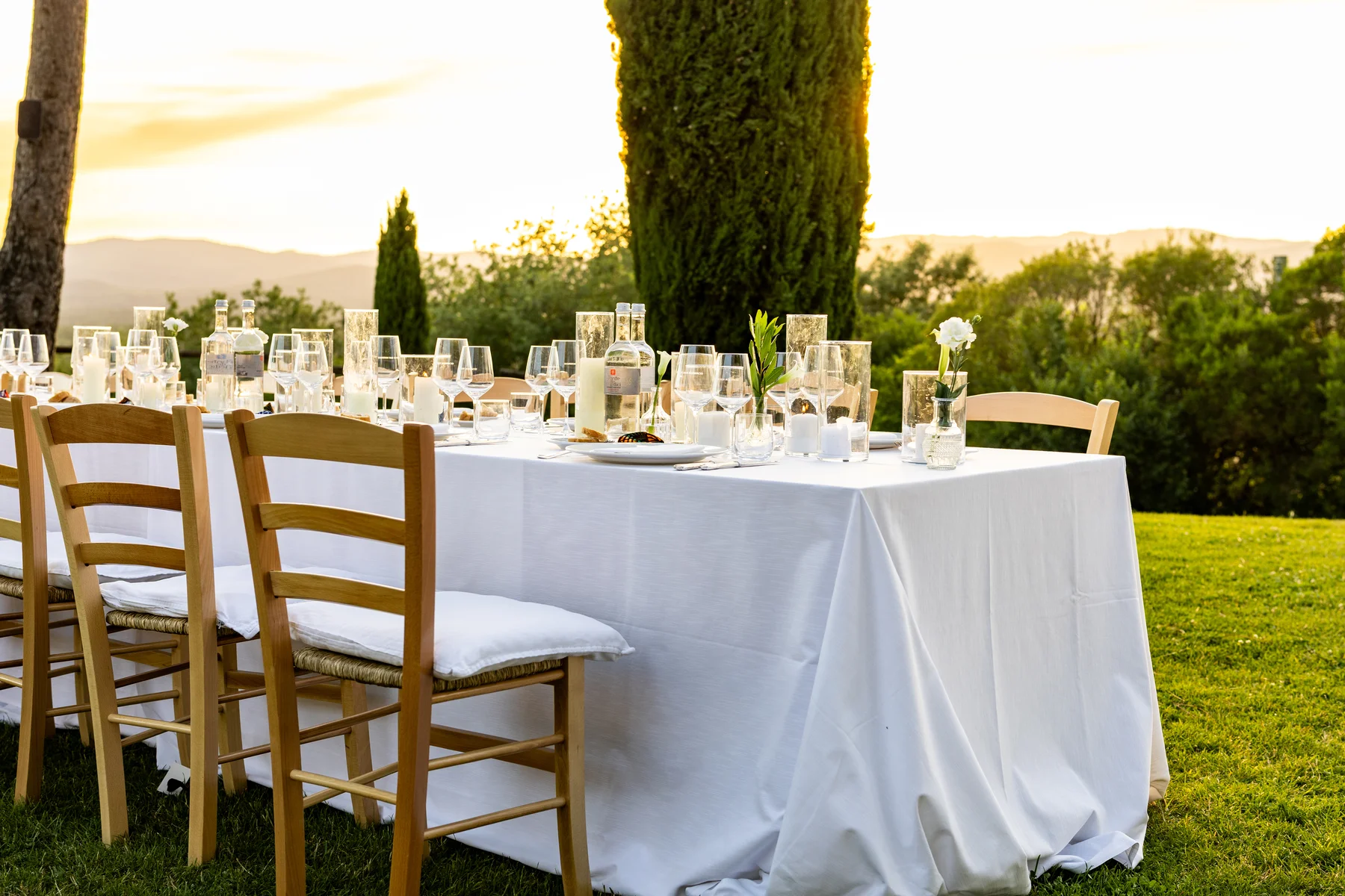 Elegant outdoor reception tablescape at Conti di San Bonifacio Wine Resort in Tuscany at golden hour, set with white linens and candles.