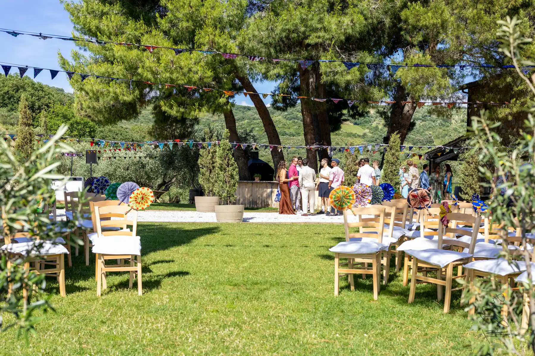 Outdoor ceremony setup at Conti di San Bonifacio in Tuscany with wooden chairs, colorful bunting, and guests mingling.