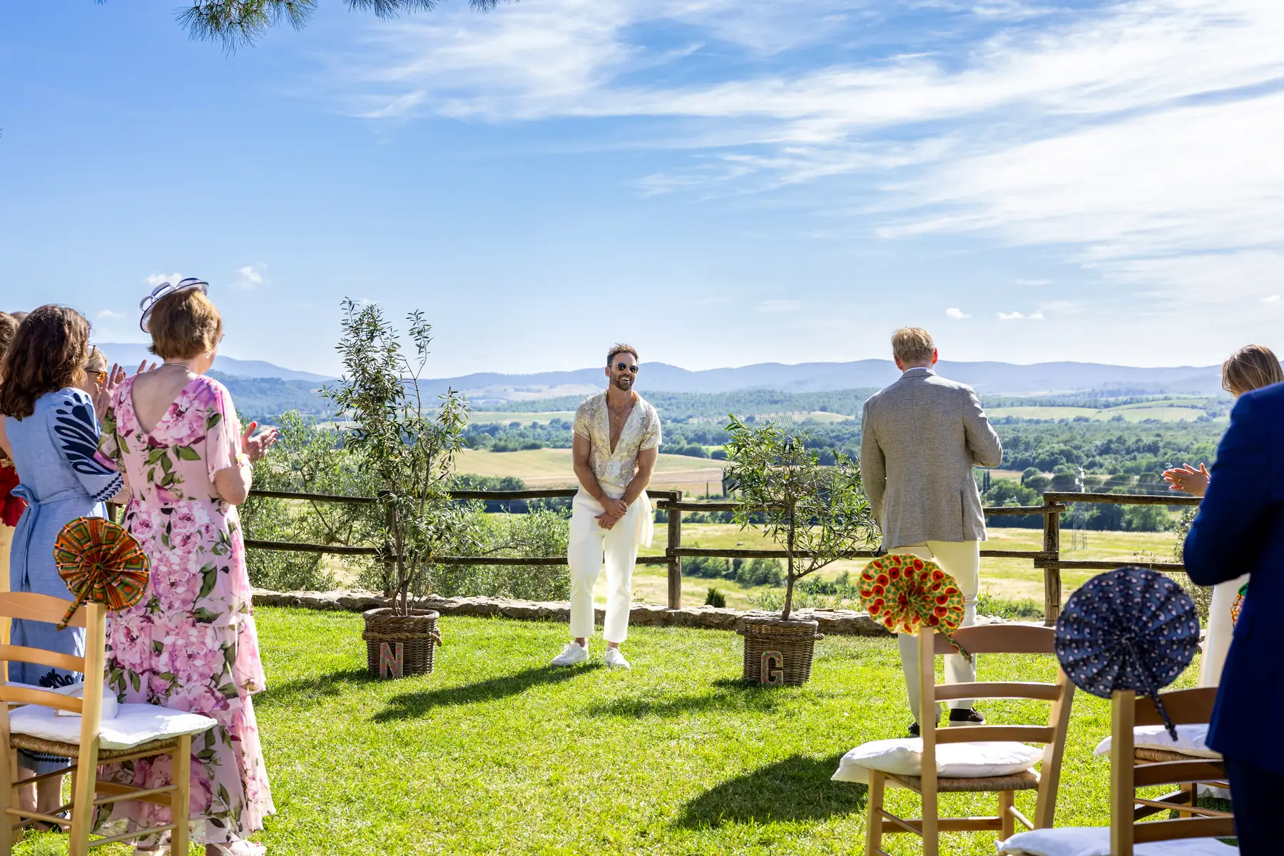 A groom in cream trousers and a floral shirt stands at the altar during an outdoor ceremony at Conti di San Bonifacio, Tuscany.
