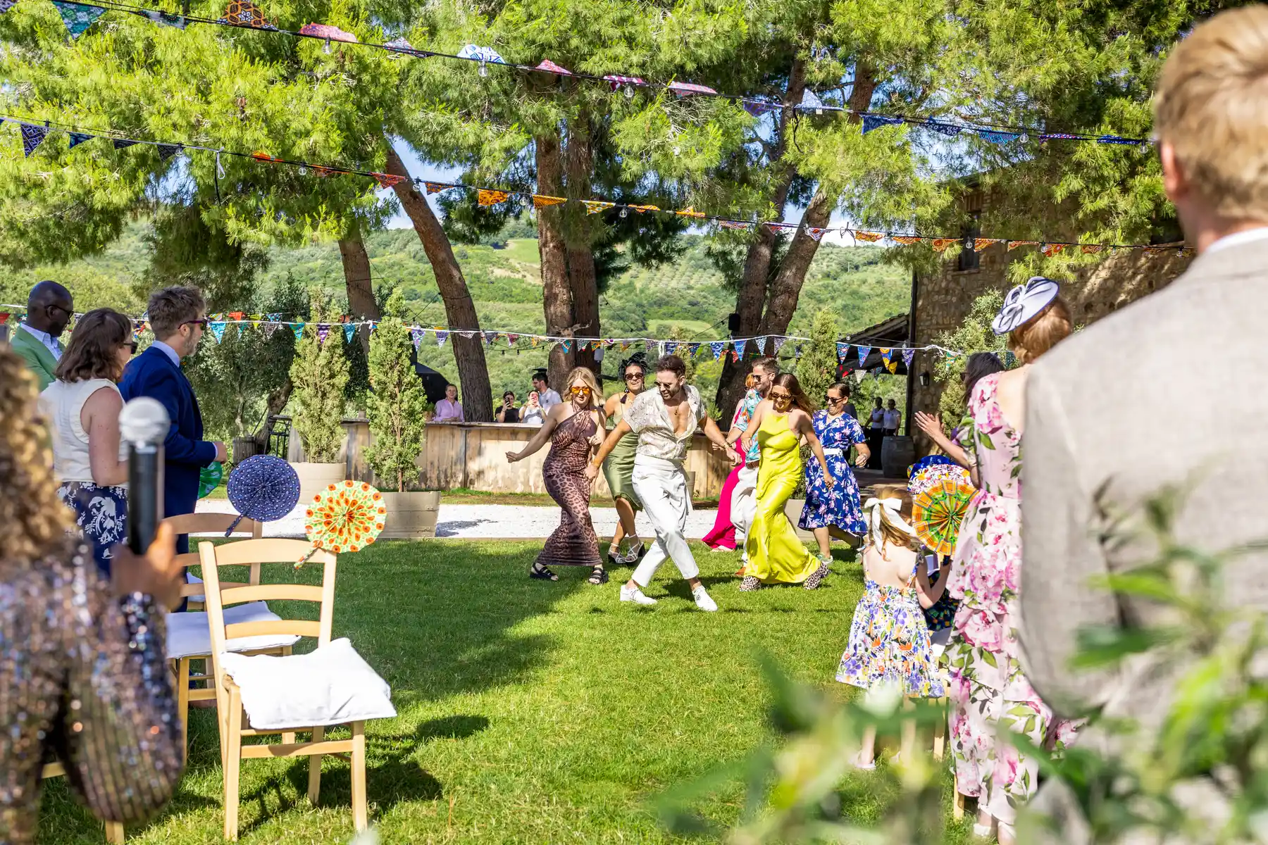 Wedding guests dance and celebrate outdoors on the lawn at Conti di San Bonifacio Wine Resort in Tuscany under colorful bunting.