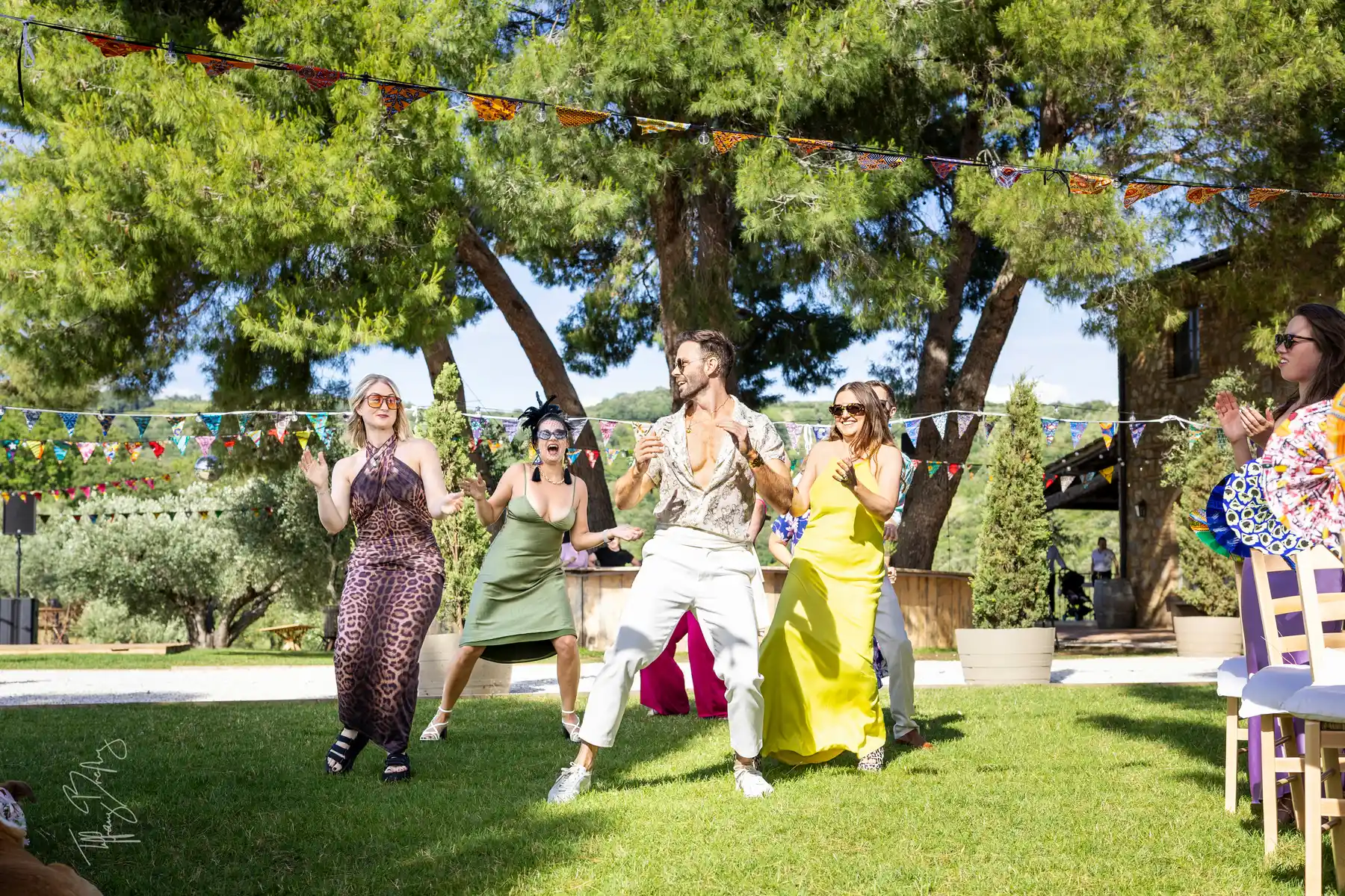 Guests dance and celebrate outdoors on the lawn at Conti di San Bonifacio Wine Resort in Tuscany during a wedding reception.
