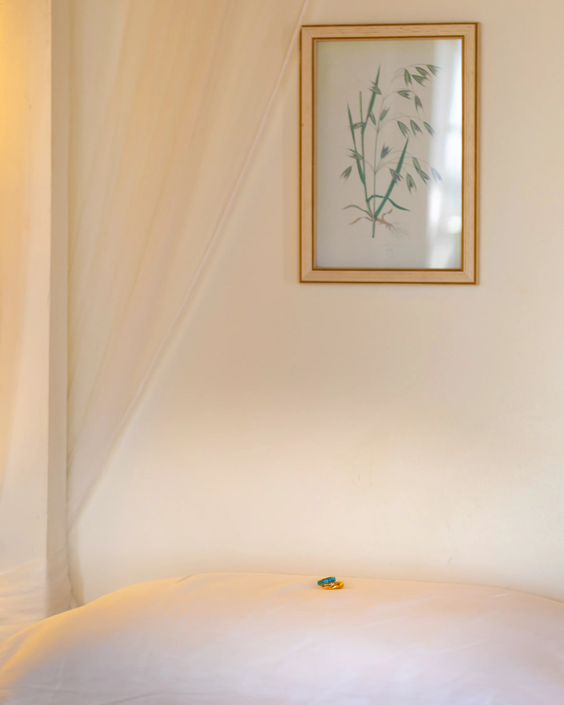 Gold rings with turquoise detail rest on white linen beneath a framed bamboo botanical print at Conti di San Bonifacio, Tuscany.