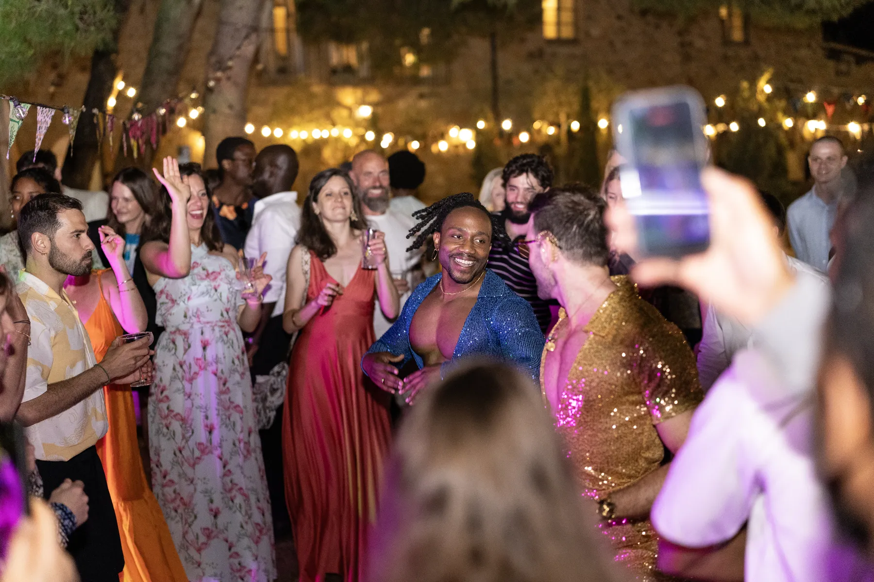 Guests and a groom in a blue sequined jacket dance and celebrate at an outdoor evening reception at Conti di San Bonifacio in Tuscany.