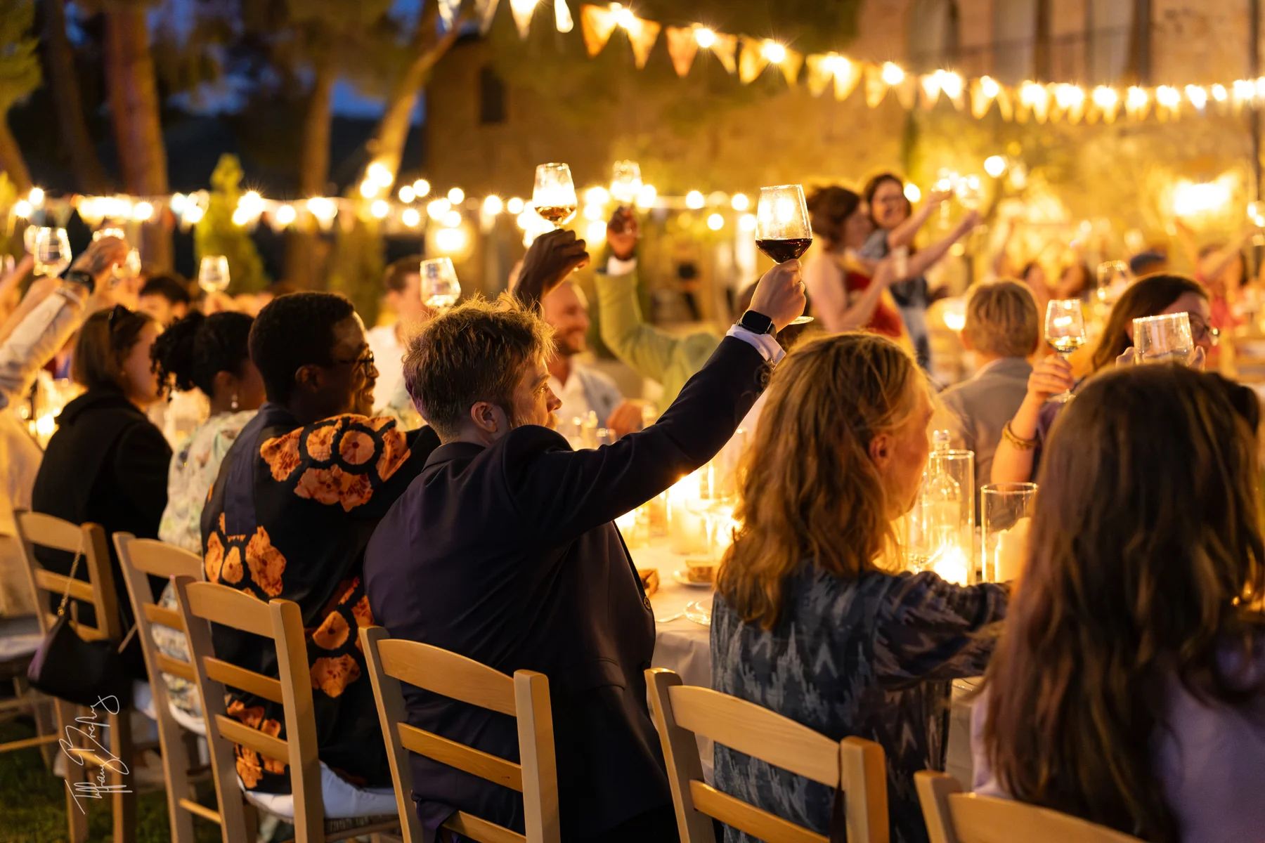 Guests raise wine glasses in a candlelit outdoor toast at Conti di San Bonifacio Wine Resort in Tuscany, Italy.