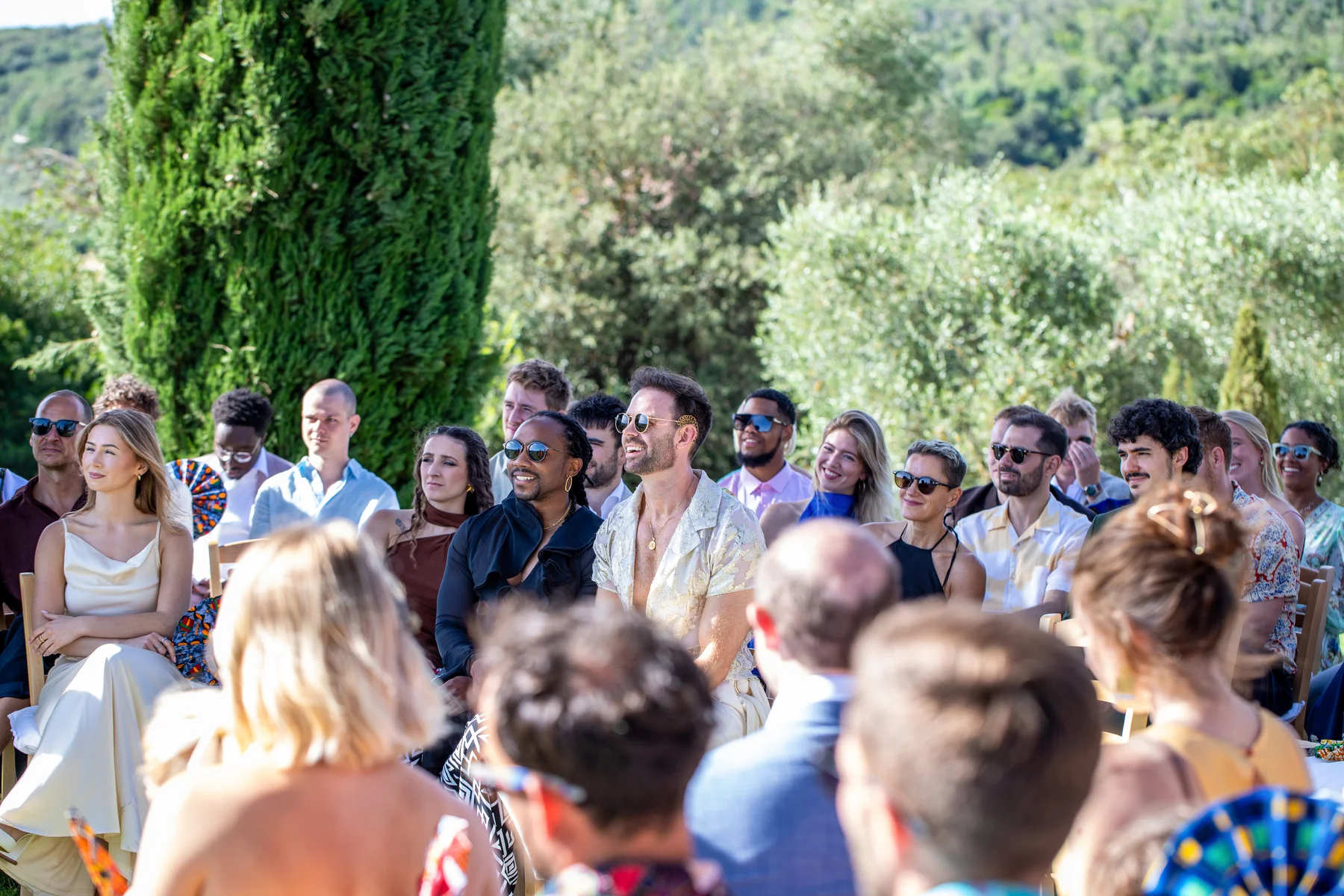 Smiling wedding guests seated outdoors at Conti di San Bonifacio Wine Resort in Tuscany, watching the ceremony unfold.