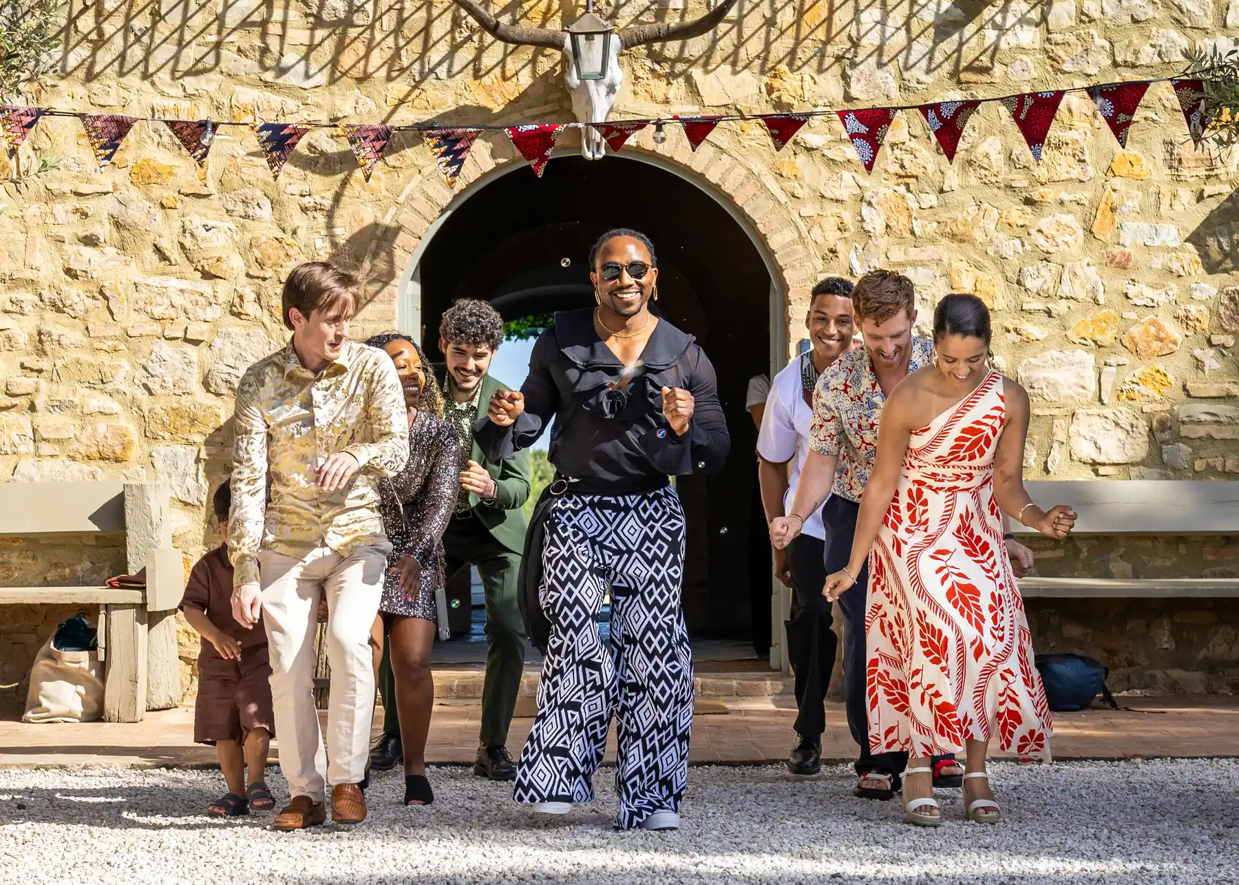 Wedding guests and grooms dance joyfully outside a stone archway at Conti di San Bonifacio Wine Resort in Tuscany.