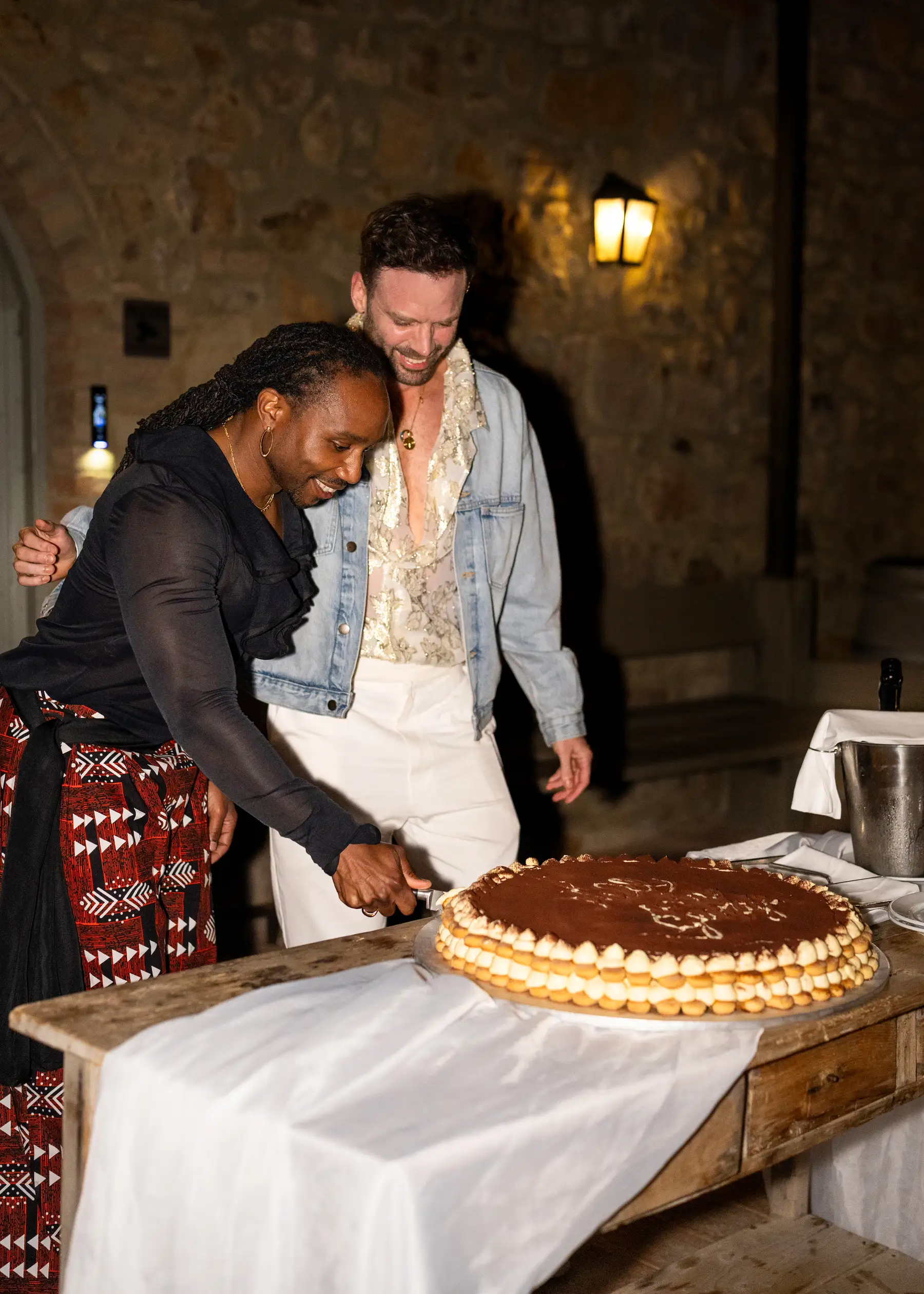 Two grooms cut a large tiramisu wedding cake at Conti di San Bonifacio Wine Resort in Tuscany, smiling together.
