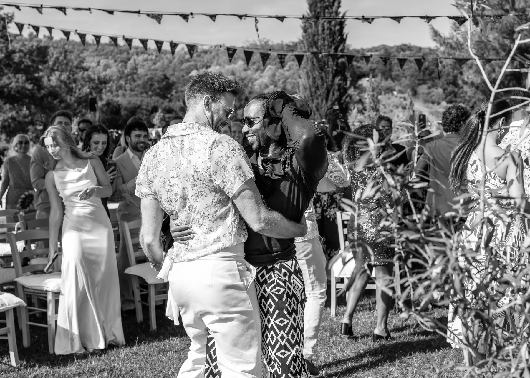 Two grooms share a joyful embrace at an outdoor wedding ceremony at Conti di San Bonifacio Wine Resort in Tuscany.