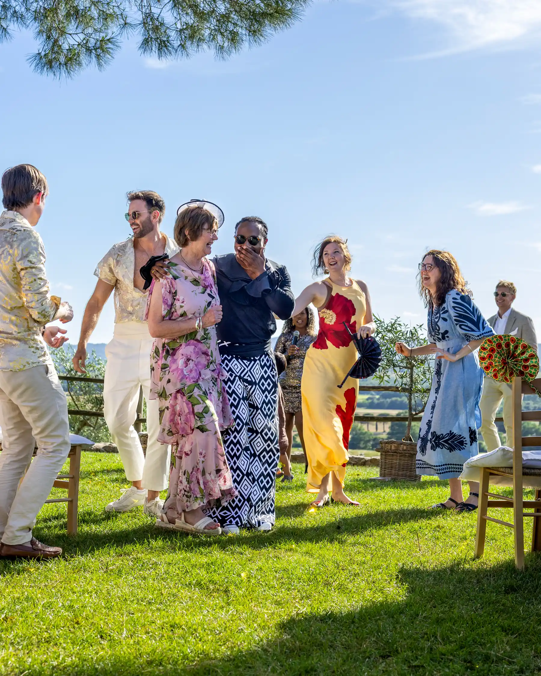 Wedding guests laugh and dance together on a sunlit lawn at Conti di San Bonifacio Wine Resort in Tuscany, Italy.