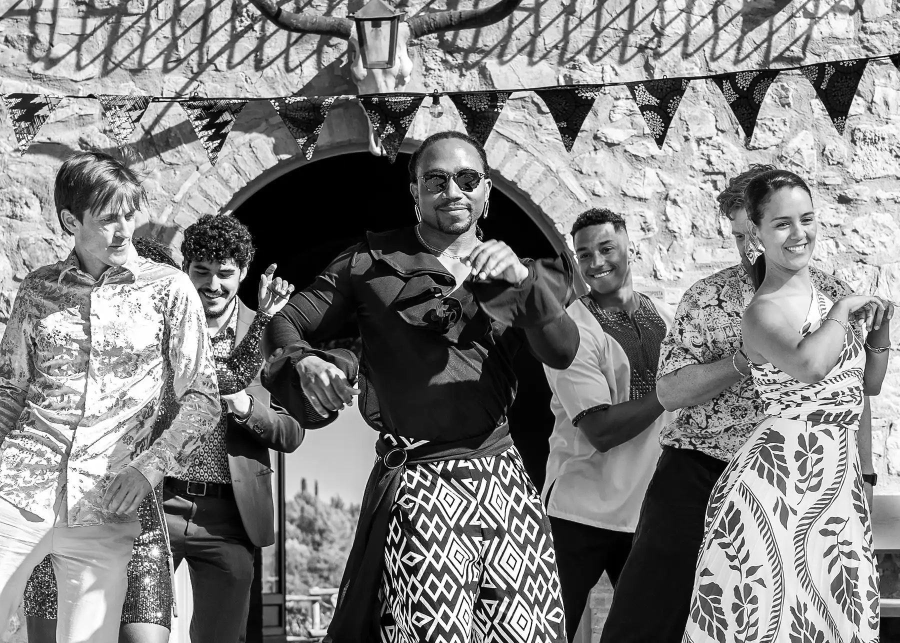 A group dances joyfully at a Tuscan reception at Conti di San Bonifacio Wine Resort, with one groom center stage in bold patterned attire.